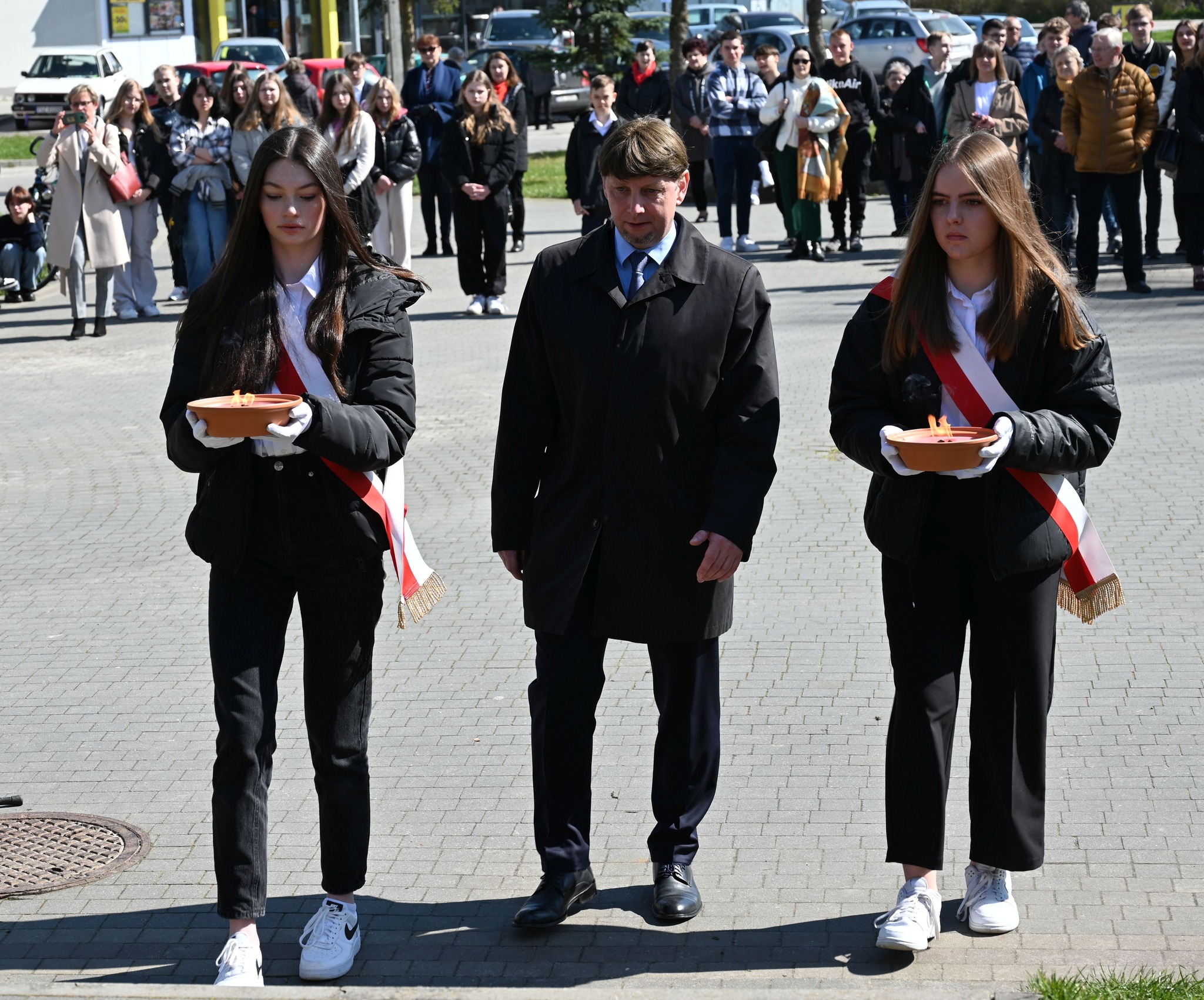 Uczennice z dyrektorem niosą symboliczny znicz