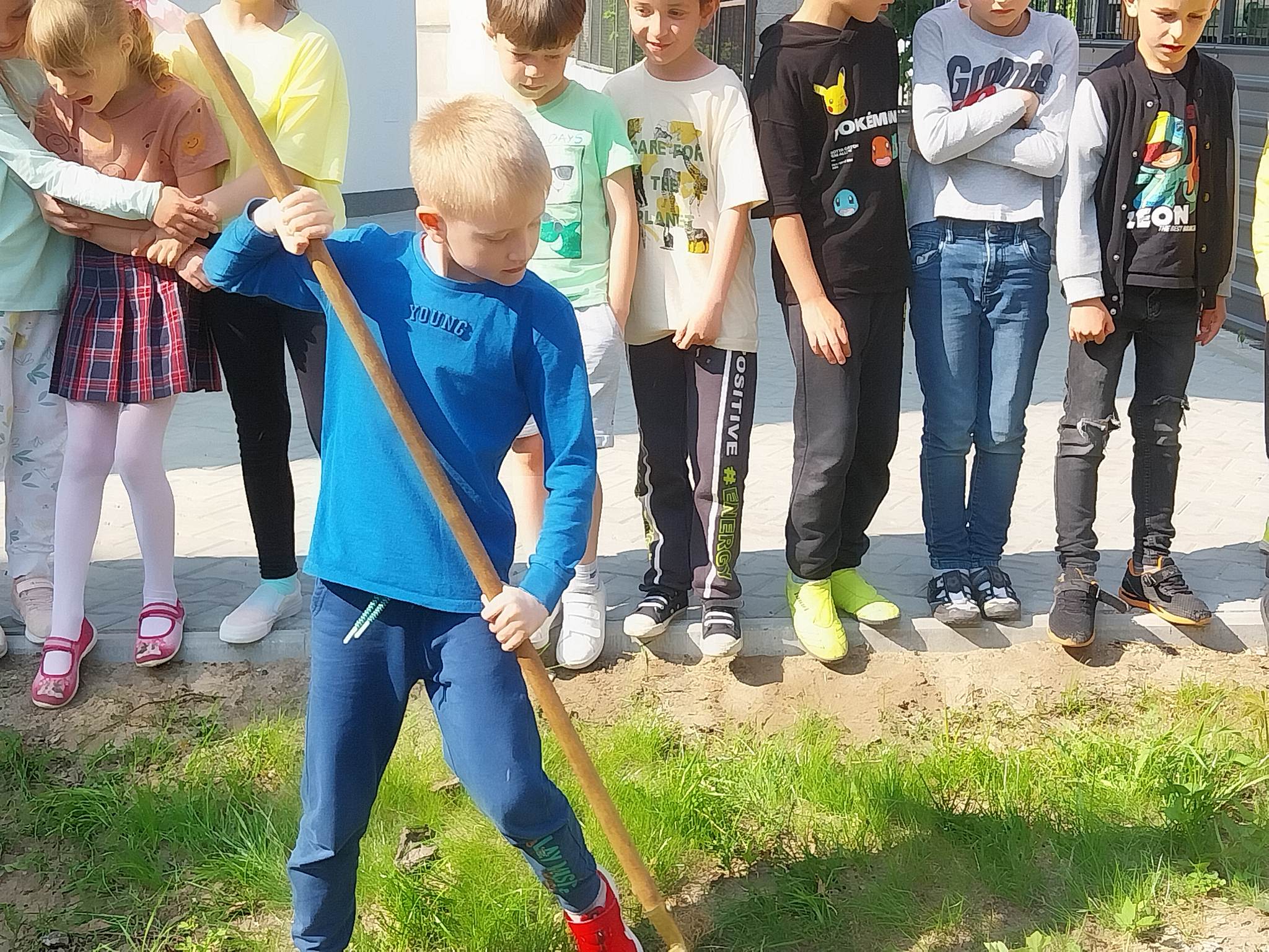 Chłopiec w niebieskiej bluzie grabi trawnik