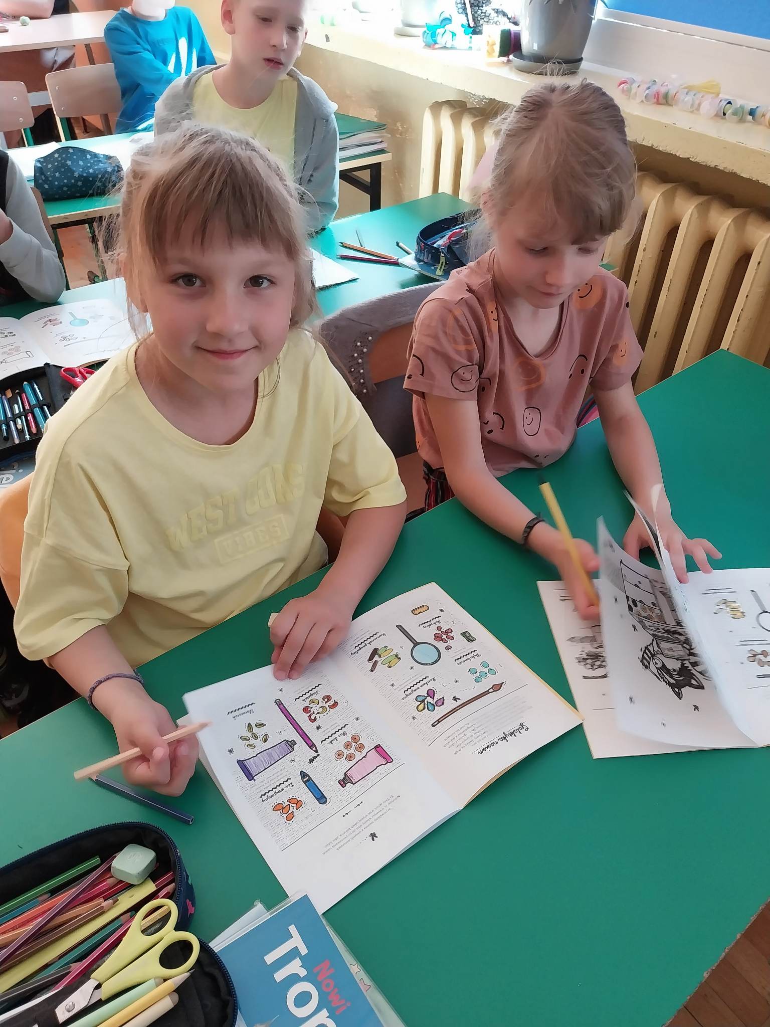 Dwie dziewczynki w ławce rozwiązują zadania w zeszytach