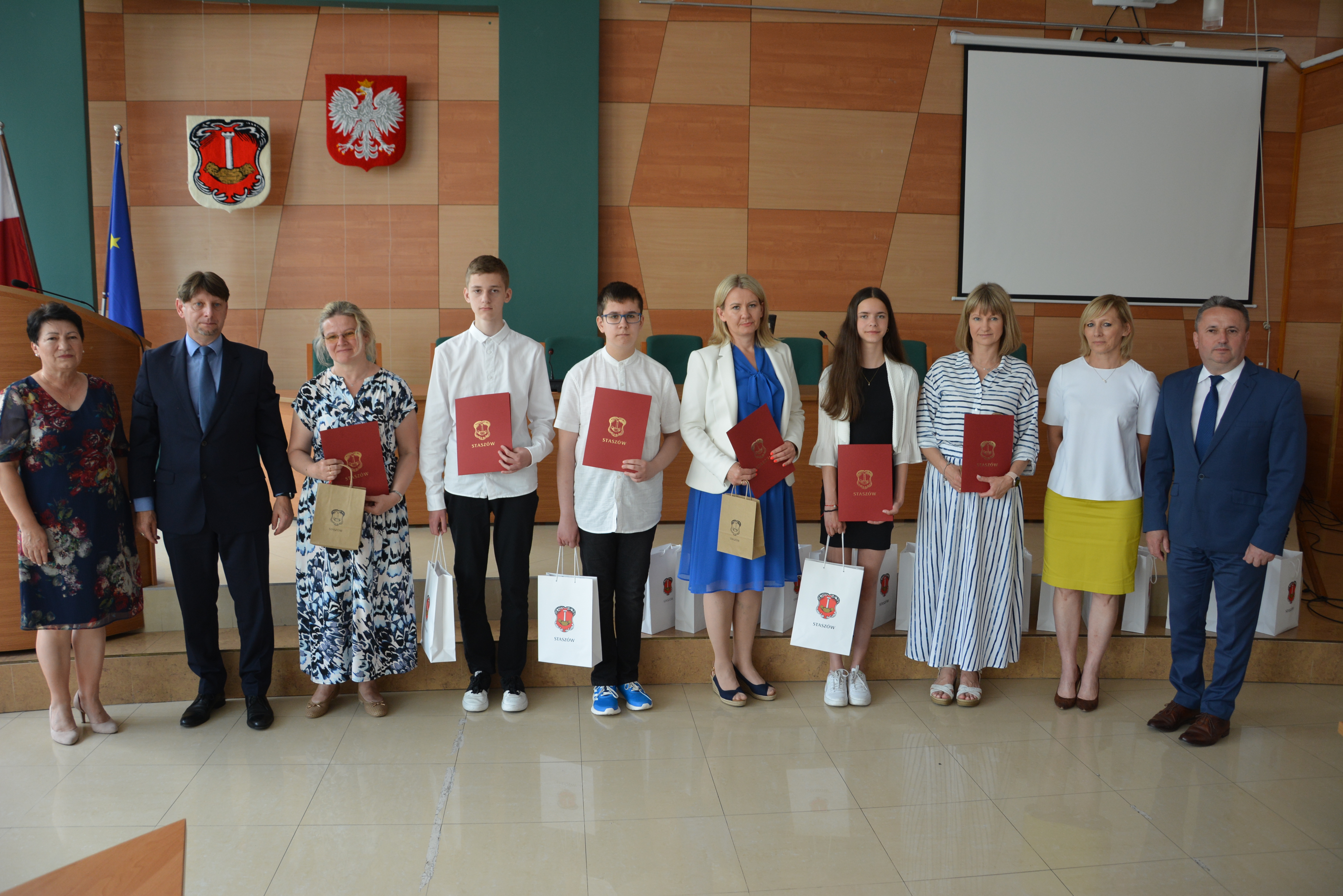 Troje uczniów i nauczycieli z dyplomami i upominkami, dyrektor, burmistrz, zastępca burmistrza, kierownik wydziału edukacji