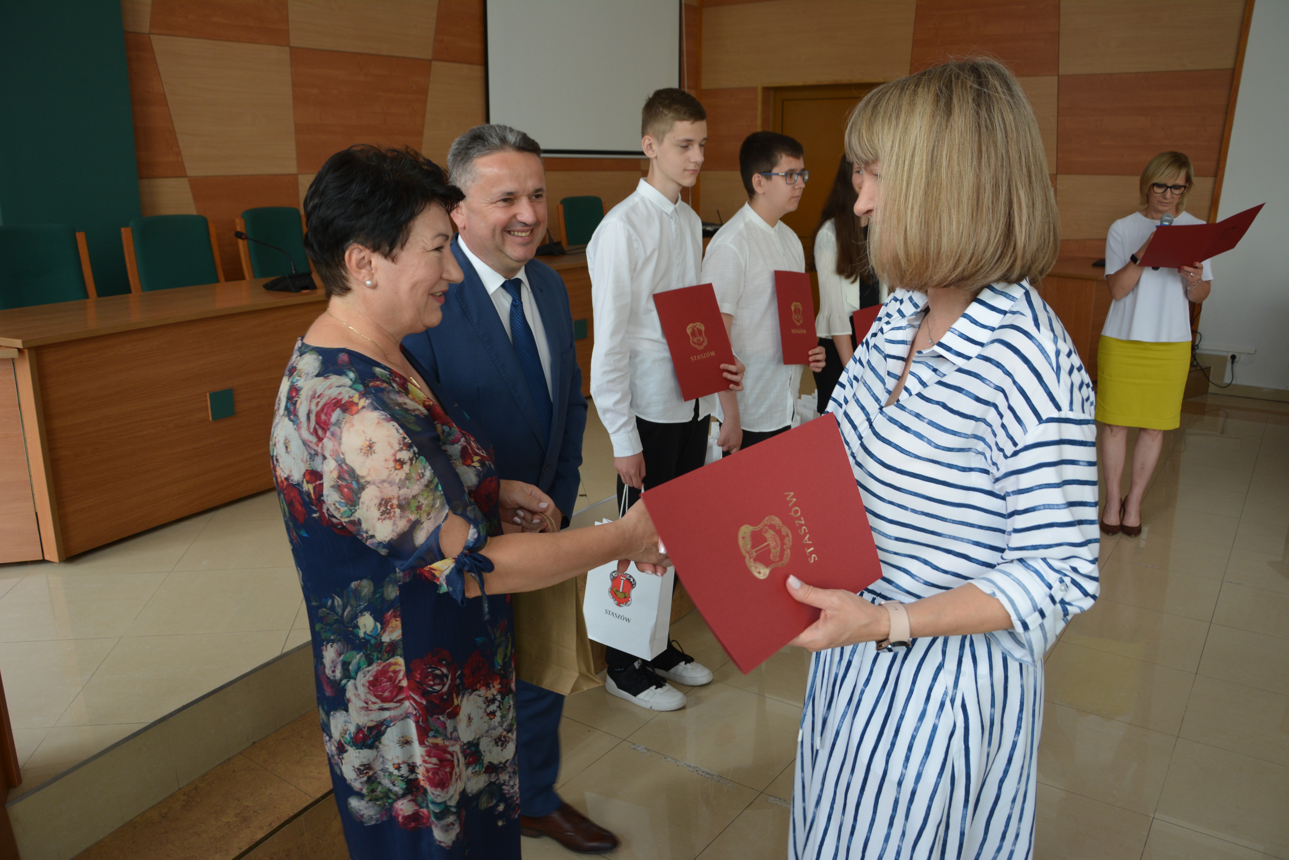 Nauczycielka odbiera dyplom i gratulacje od burmistrza i pani kierownik wydziału edukacji