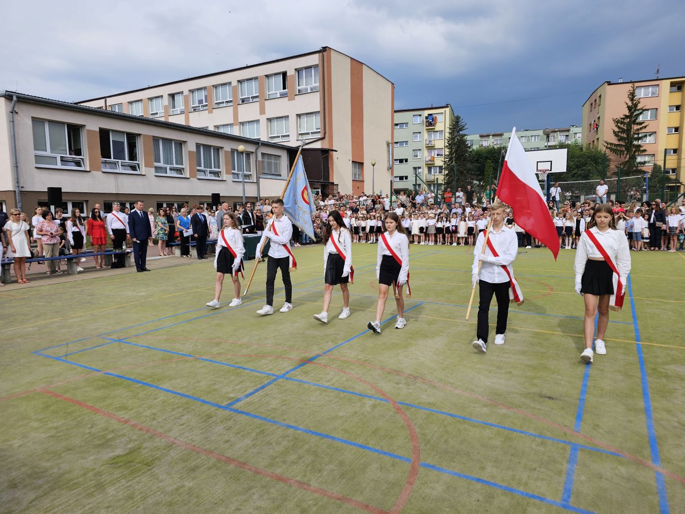 Wprowadzenie pocztu sztandarowego, boisko szkolne, w głębi uczniowie, dyrekcja, nauczyciele