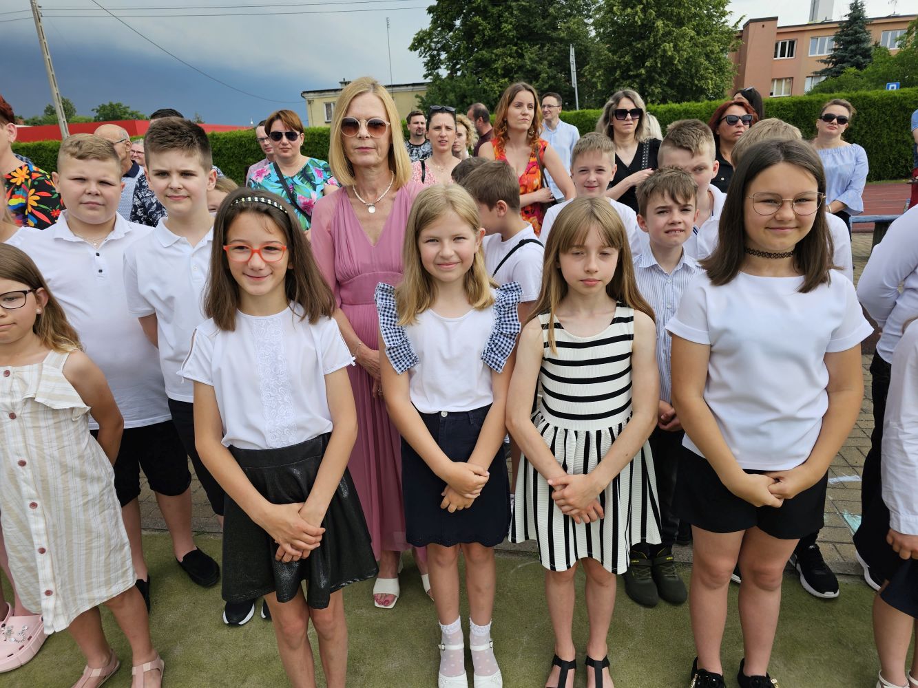 Grupa uczniów klas młodszych z wychowawczynią, za nimi rodzice